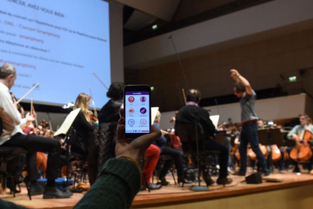 A woman holds a smartphone on January 19, 2018 during a rehearsal at the Orchestre national de Lille (national orchestra of Lille) in the French northern city of Lille, where the public can interact with his mobile phone. 