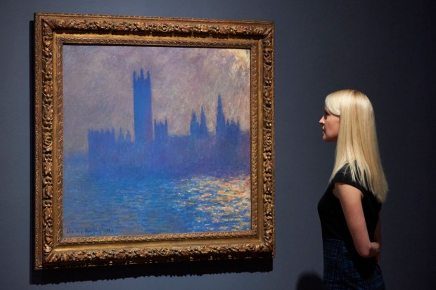 A woman poses by a painting of the Houses of Parliament by French artist Claude Monet during a press preview for the exhibition French Artists in Exile (1870-1904) at Tate Britain in London on October 30, 2017 